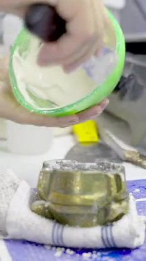 Diş teknisyeninin, yeşil bir kaseden diş yapısını kalıba dökmek için karışık alçı taşıdığı yakın plan..