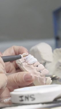 Bir diş teknisyeninin, laboratuvar ortamında bir diş protezinde seramik oluşturmak için fırça kullanırken yakın plan fotoğrafı..