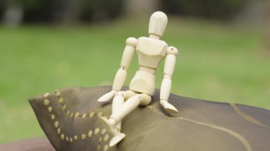 Eklemli ahşap manken, yumuşak odaklı çimenli bir arka planı olan süslü bir yastığın üzerinde duruyor..