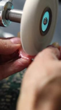 Laboratuvar ortamında döner parlatma makinesi kullanarak yapay bir protezi cilalayan bir diş teknisyeninin yakın çekimi..