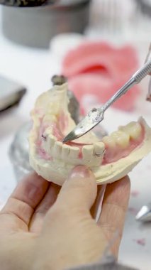 Diş teknisyeninin diş laboratuarında metal bir aletle sıva modelinin protezini rafine ettiği yakın plan..