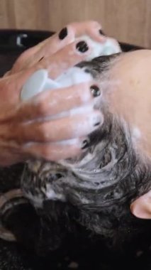 Kuaför lavabosunda saçlarını yıkadığı sırada müşterilerine masaj yapan bir stilistin yakın plan fotoğrafı..