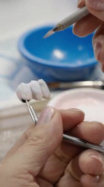Diş teknisyeninin elleri, bir laboratuvar ortamında dişçiye diş bakımı için seramik kaplama yontmak için hassas bir araç kullanıyor..