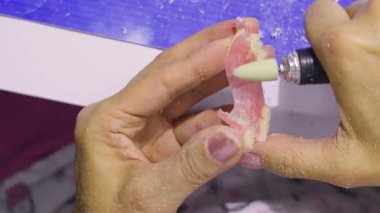 Diş teknisyeninin diş laboratuarı tezgahında pembe çıkarılabilir kısmi protezi düzleştirmek için dönme alet kullanırken yakın plan görüntüsü..