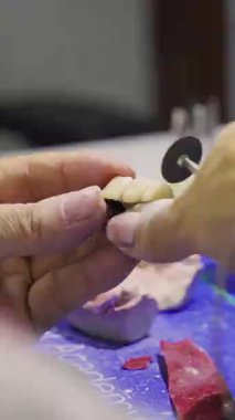 Bir diş teknisyeninin elleri protez dişleri şekillendirmek ve cilalamak için döner bir alet kullanır..