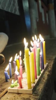 Bir grup insan, karanlıkta huzur içinde yanan parlak renkli mumların etrafında toplanıyor..
