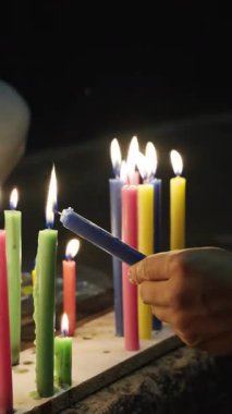 Bir el, başka bir alevden mavi bir mum yakar. Renkli mumlarla dolu bir gece toplantısında..