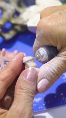 Bir laboratuvar ortamında yapay dişleri öğütmek ve cilalamak için dönen bir alet kullanan bir diş teknisyeninin elleri.