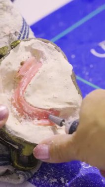 Diş teknisyeninin, alçı kalıbının içinde dönen bir aletle alt protezin pembe balmumu tabanını rafine ettiği yakın plan..