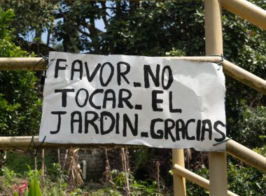 İspanyolcada yıpranmış ahşap tabela, ziyaretçileri doğal bir manzaraya karşı bahçeye dokunmamaya teşvik ediyor.