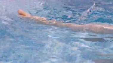 Suda yüzen yüzücü, parlak, berrak bir yüzme havuzunda ayak ve bacak hareketleriyle dalgalanmalar yaratır..