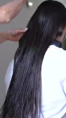 Yaşlı eller genç bir kadının düz, siyah saçlarını büyük bir tahta fırça kullanarak dikkatlice tarıyor..