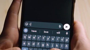 Metin ve semboller kullanarak romantik bir mesaj yazarken akıllı telefonu tutan ellerin yakın çekimi.