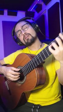 Kulaklık ve gözlük takan sakallı adam ses geçirmez bir stüdyoda klasik gitar çalıyor..