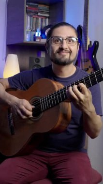 Neşeli müzisyen, enstrümanlar ve sıcak aydınlatmalarla çevrili rahat bir ev stüdyosunda klasik gitar çalar..