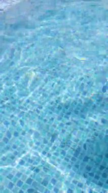 Açık mavi yüzme havuzu suyuna yakın çekim güneş ışığı döşeme üzerinde dalgalanmalar ve yansımalar yaratır..