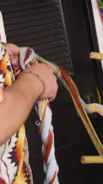 Geleneksel tekstil dokuma sürecinin bir parçası olan dokuma tezgahında renkli iplikler düzenleyen zanaatkar ellerin yakın çekimi.