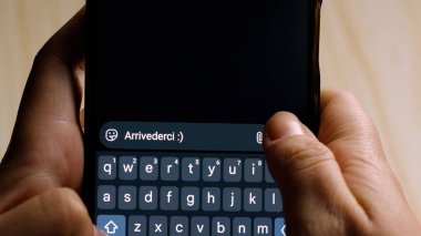 Bir mesajlaşma uygulamasında arrivederci yazarken akıllı telefonu tutan ellerin yakın çekimi.