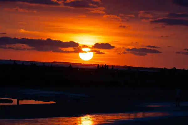 İnsanlar gün batımında sahilde.