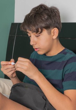 Genç bir çocuk siyah bir çantada eli ile bir yatakta oturuyor.