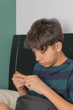 Bir çocuk yatakta oturuyor ve kalemle oynuyor.