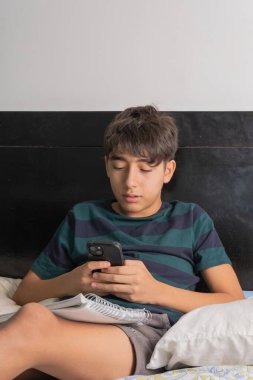 Telefon ve okul defteriyle birden fazla iş yapan genç bir çocuk.