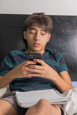 Bir çocuk elinde cep telefonuyla yatakta oturuyor.