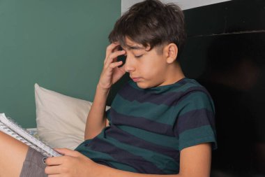 Bir çocuk yatakta yatarken kitap okuyor.