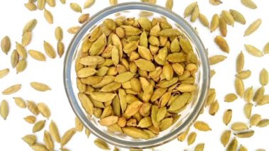 Etrafına cam bir kase içindeki yeşil kakule döküldü, beyaz arka plan, merkez çerçeve, üst görüş, kapalı otlar ve baharatlar üzerinde dönen