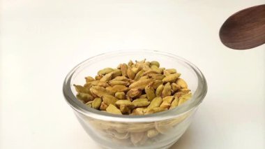 Spoon out of Green cardamom pods from the glass bowl with a wooden spoon, herbs and spices