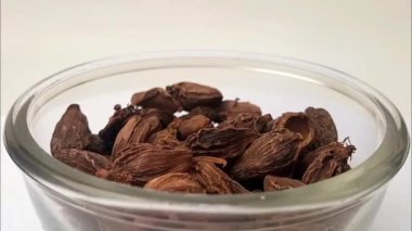 Büyük kakule ya da siyah kakule beyaz arka planda bir cam kaseye düşer, büyük kakule dolu bir cam kase ya da ortada siyah kakule, döner, mikro shot, şifalı bitkiler ve baharatlar