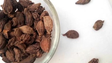 Çemberin yarısı şekilli büyük kakule ya da siyah kakule cam kaplar etrafına saçılmış, çerçevenin sol yarısı, dönüşümlü, beyaz arka plan, yakın plan, otlar ve baharatlar