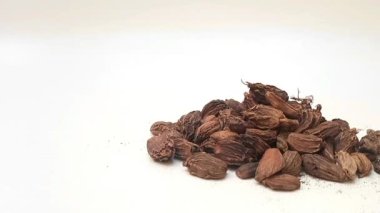 Beyaz zemin üzerinde büyük kakule yığını ya da siyah kakule izole edilmiş, sağdan sola hareket eden, önden bakan, kapalı otlar ve baharatlar