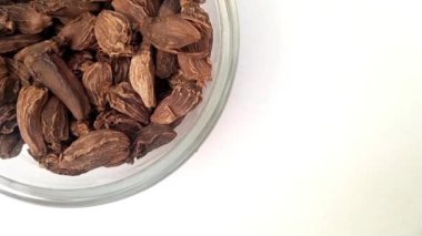 Büyük kakule ya da siyah kakule sol üst köşede izole edilmiş vaziyette, büyük kakule dolu bir cam kase ya da beyaz arka planda siyah kakule, yakın plan, bitkiler ve baharatlar