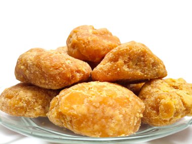 Jaggery ya da Gur parçaları cam bir plaka içinde temiz beyaz bir arka plan, izole edilmiş mikro çekim. Cam tabaktaki organik kahverengi şeker parçaları izole edilmiş.