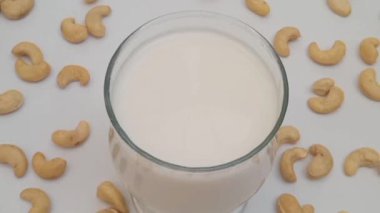 Beyaz arka planda bir bardakta vejetaryen kaju sütünden zum yap. Sağlıklı süt sütü alternatifi. Kaju fıstığı tüm yüzeye yayılmış.