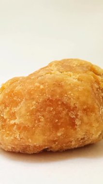 Beyaz arka planda dönen bir parça Jaggery ya da Gur izole edilmiş, yakın plan. Organik kahverengi kamış şeker parçası dikey izole