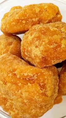 Camdaki organik jaggery ya da Gur parçaları temiz beyaz arka plan, üst manzara, izole edilmiş. Cam kasedeki kahverengi kamış şeker parçaları dikey izole edilmiş.
