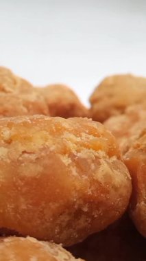 Beyaz arka planda dönen Jaggery ya da Gur parçalarının mikro görüntüsü. Kahverengi organik şeker parçaları dikey