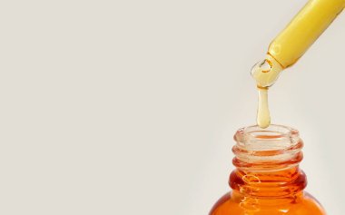 Şişeden damlayan sıvı sarı-turuncu C vitamini ya da beyaz arkaplanda retinol serumu, kapat.