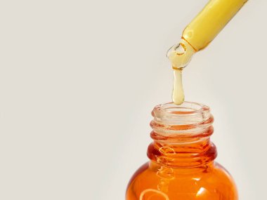 Şişedeki pipeti kapat. Sıvı sarı-turuncu C vitamini damlat. Ya da beyaz arka plana retinol serumu damlat.