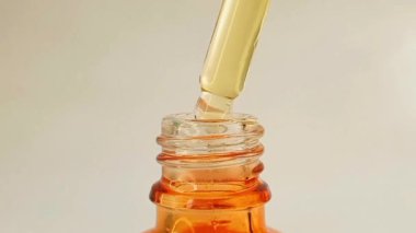 Şişe pipeti damlatıcısını çıkarıp beyaz arka planda hafif sarı-turuncu C vitamini ya da retinol serumu damlatırken mikro çekim