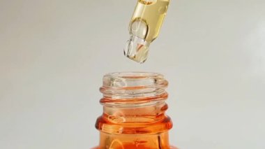 Beyaz zemin üzerinde mikro şişe pipet damlası sıvı sarı-turuncu vitamin c veya retinol serumu.