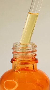 Şişe pipeti damlatıcısını çıkarıp beyaz arka planda hafif sıvı sarı-turuncu C vitamini ya da retinol serumunu damlatıyor.