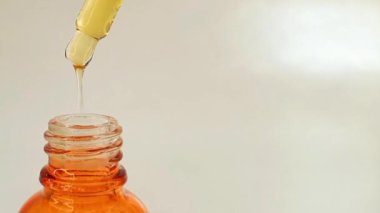 Şişe pipeti damlatıcısını çıkarmak ve damlatan yapışkan sıvı sarı-turuncu C vitamini veya beyaz arka planda retinol serumu, çerçevenin sol tarafında.