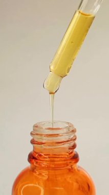 Beyaz arka planda şişe pipeti damlatıcısı ve damlayan yapışkan sıvı sarı-turuncu vitamin c veya retinol serumu, dikey klips