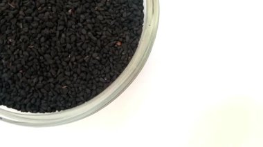 Siyah kimyon tohumları ya da siyah kimyon tohumları cam bir kasenin sol üst köşesinde izole edilmiş, siyah kimyon tohumlarıyla dolu bir cam kase ya da beyaz arka planda siyah kimyon tohumları, kapatın, bitkiler ve baharatlar