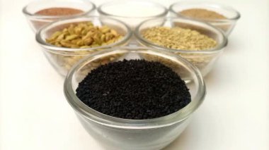 Bir kase siyah kimyon tohumuna ya da aromatik baharat çeşnili siyah kimyon tohumlarına ve arka plandaki cam kaselerde bitkilere odaklanmak.