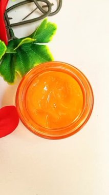 Cam bir kaptaki C vitamini kremi beyaz arka planda izole edilmiş, yakınlaştırıyor. Sarı-turuncu C vitamini kremi gibi hafif jel. Üst görünüm, dikey klip
