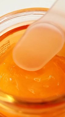 Cam bir kutudan C vitamini kremi alıyorum. Beyaz arka planda sarı-turuncu C vitamini kremi gibi hafif jel. dikey klip